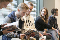 vier Männer und eine Frau sitzen auf einer Bank und schauen in Broschüren