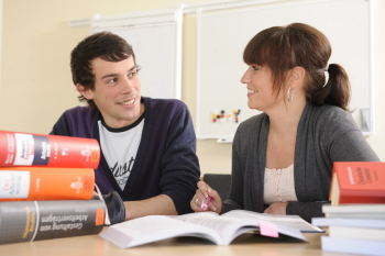 Ein Student und eine Studentin des Fachbereichs Wirtschaft und Gesundheit lesen Bücher und unterhalten sich über den Lesestoff.