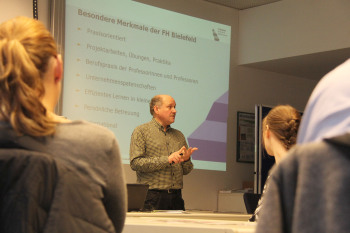 Im Bildhintergrund steht Prof. Keuntje vor einer Wandprojektion mit den Merkmalen der FH-Bielefeld. Im Vordergrund sind die Zuhörer zu sehen.