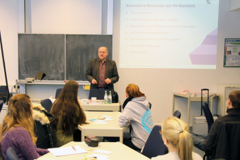 Seminarsituation mit Mann vor einer Tafel und Menschen im Vordergrund