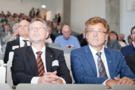 Prof. Dr. Christian Schröder und Prof. Dr. Friedrich Biegler-König sitzen auf Sitzen im Audimax.