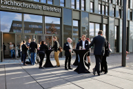 Menschen stehen an Stehtischen vor dem FH-Eingang an Konferenzbereich