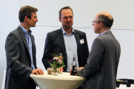 Drei Männer stehen an einem Tisch im Konferenzbereich der FH.