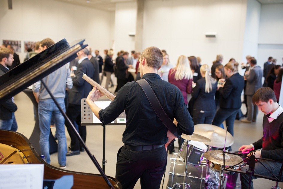 Musiker mit Instrumenten im Vordergrund, Menschen im Hintergrund.
