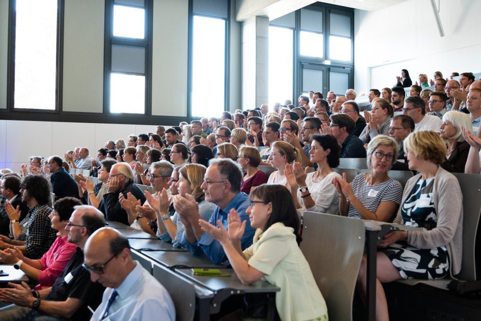 Viele Menschen sitzten im Audimax und Applaudieren