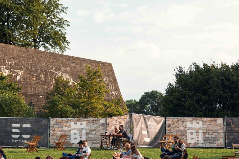Blick auf die Burgmauern der Sparrenburg, im Vordergrund sitzen Personen an Tischen und blicken Richtung Bühne.