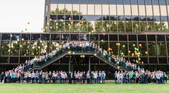 Gruppenbild vor Gebäude, die Personen lassen bunte Lutballons aufsteigen