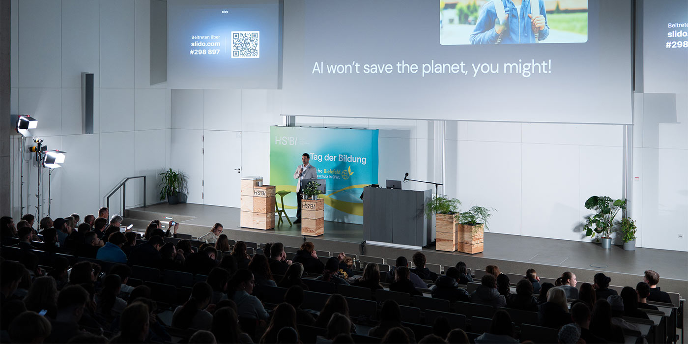 Das vollbesetzte Audimax von hinten, auf der Bühne steht ein Mann