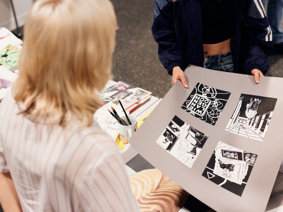 Eine Frau zeigt eine Mappe mit Zeichnungen