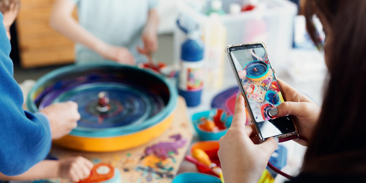 Eine Person fotografiert mit einem Handy eine bunte Farbscheibe