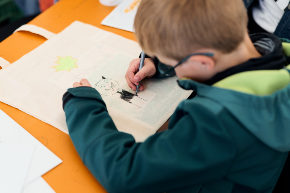 Ein Junge malt mit Stiften auf einem Stoffbeutel