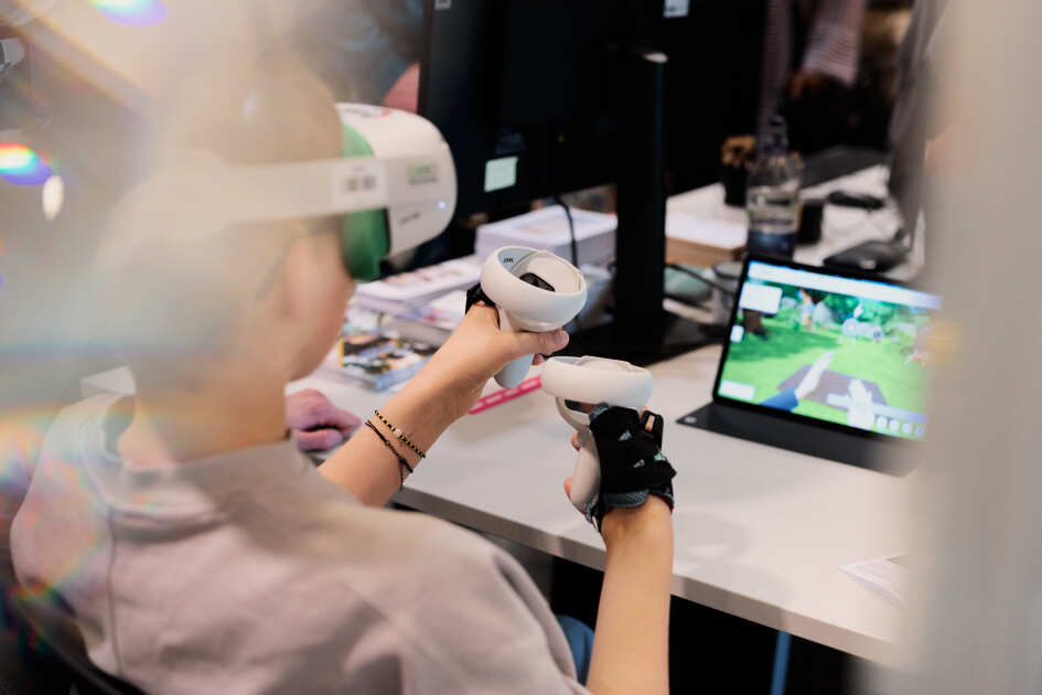 Foto: Ein Kind trägt eine VR Brille und sitzt an einem Tisch mit Kontrollern in der Hand