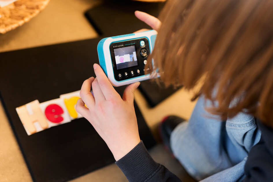 Foto: Ein Kinde fotografiert mit einer Print Kamera seinen Namen um daraus ein Namensschild zu machen