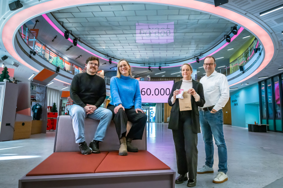 Foto: Zwei Pesonen sitzen auf einem Sofa in der Wissenswerkstadt, daneben stehen zwei Personen, im Hintergrund sieht man die Zahl 60000 auf einem Bildschirm