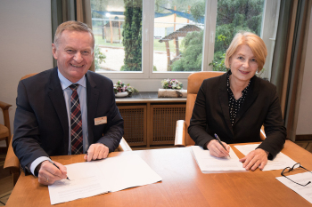 GEorg Rüter und Ingeborg Schramm-Wölk sitzen hinter eine Tisch und unterzeichnen jeweils ein Papier