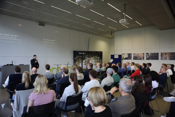 Menschen sitzen im Konferenzbereich der HSBI, vorne steht ein Mann und spricht in ein Mikrofon