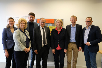 Drei Frauen und vier Männer stehen vor einer Wand