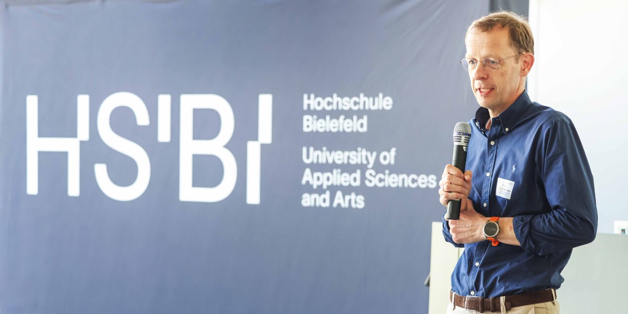 Der Vizepräsident der Hochschule Bielefeld Prof Dr Ulrich Schäfermeier steht vor einer Wand mit der Aufschrift HSBI