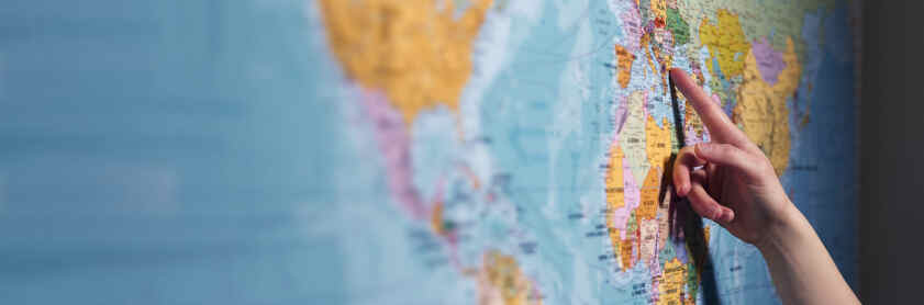 A hand is pointing at a map of the world