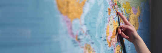Eine Hand zeigt auf eine Weltkarte