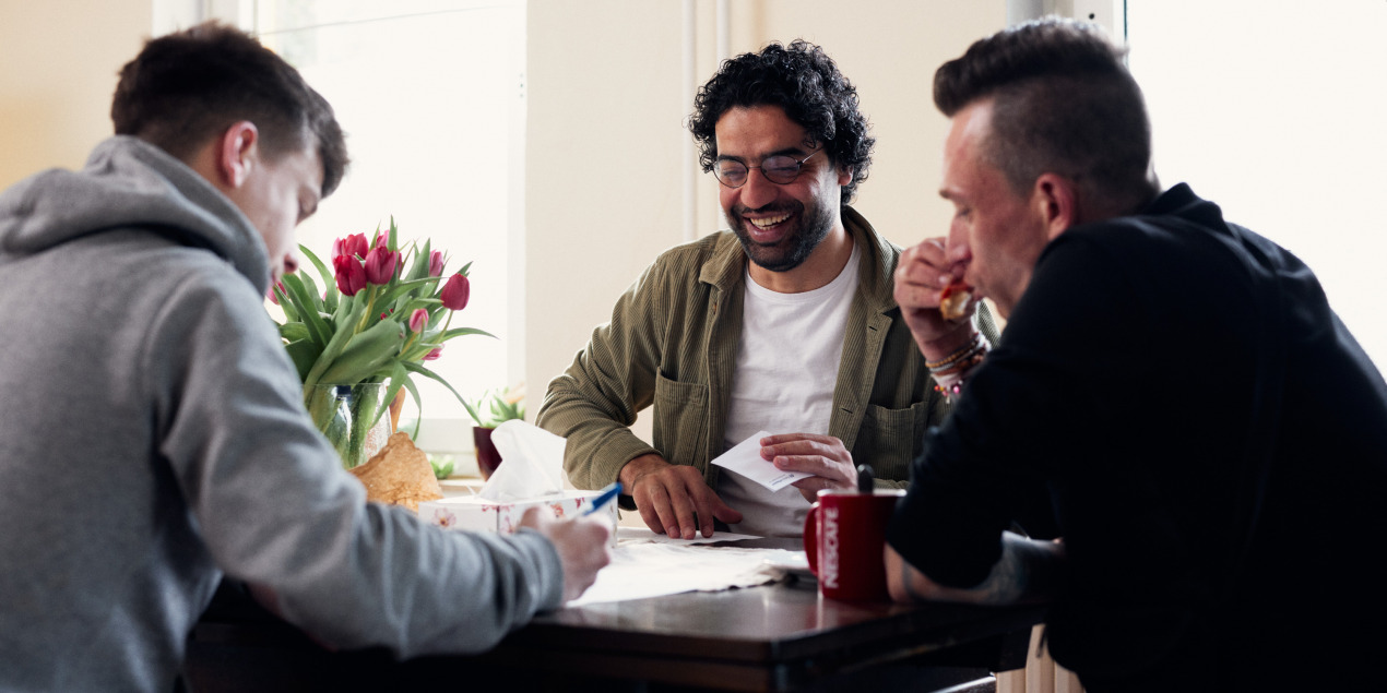 Ahmed Alkhateeb sitzt an einem Tisch mit zwei Männern Sie füllen gemeinsam Formulare aus