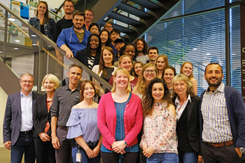Gruppe an Personen, männlich und weiblich, steht vor und auf einer Treppe.