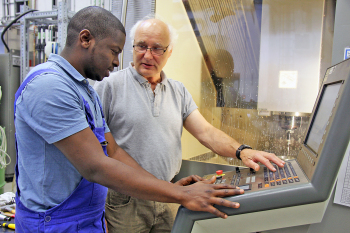 Foth und Sow stehen an dem Bedienfeld einer CNC-Dreh- und Fräsmaschine.