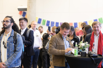 Mehrere Personen stehen an Stehtischen im Konfernezbereich und schauen zur Bühne