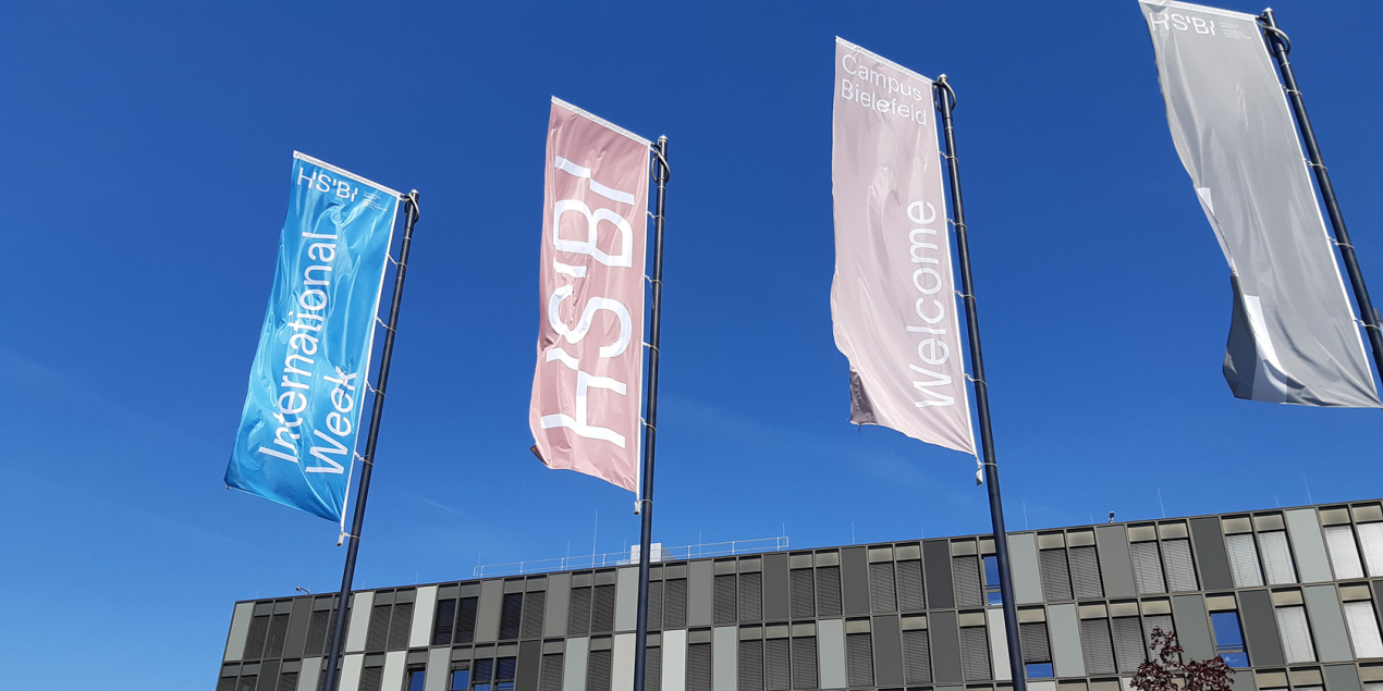 Vier Flaggen vor dem Hauptgebäude der HSBI auf einer steht International Week