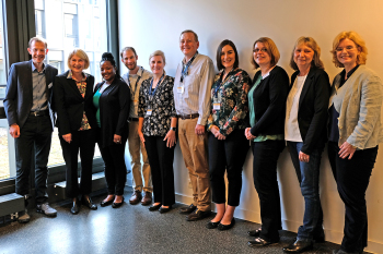 Zehn Personen stehen nebeneinander vor einer Wand und blicken in die Kamera.