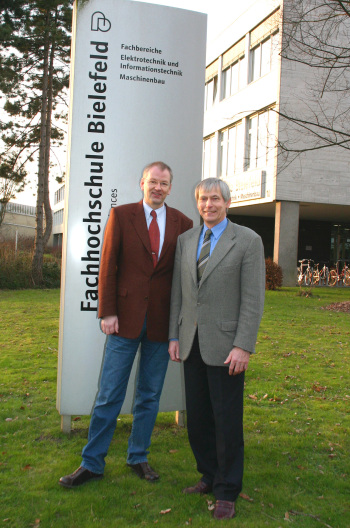 Jaroscheck und Zenke stehen vor eine Stehle der Fachhochschule Bielefeld.