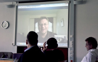 Prof. Dr. Christian Schröder ist im Hintergrund auf einer Leinwand zu sehen, währen die Senatmitglieder im Vordergrund sitzen.