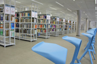Im Vordergrund stehen blaue Stühle vor den regalen mit den Büchern.