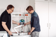 Zwei Männer betrachten einen Versuchsaufbau im Labor für angewandte Informatik