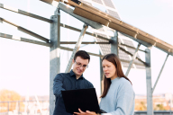 Zwei Personen stehen mit einem Laptop auf dem Dach der HSBI vor der Solaranlage