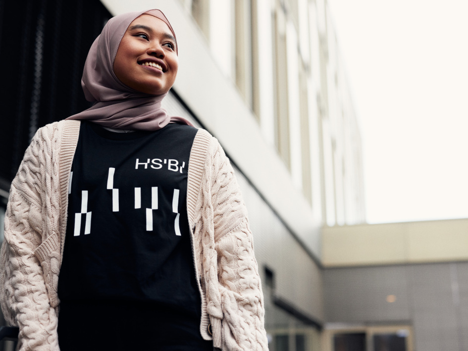 Eine junge Studierende, die ein T-Shirt mit dem HSBI-Logo trägt, geht durch den Innenhof des Hauptgebäudes der HSBI