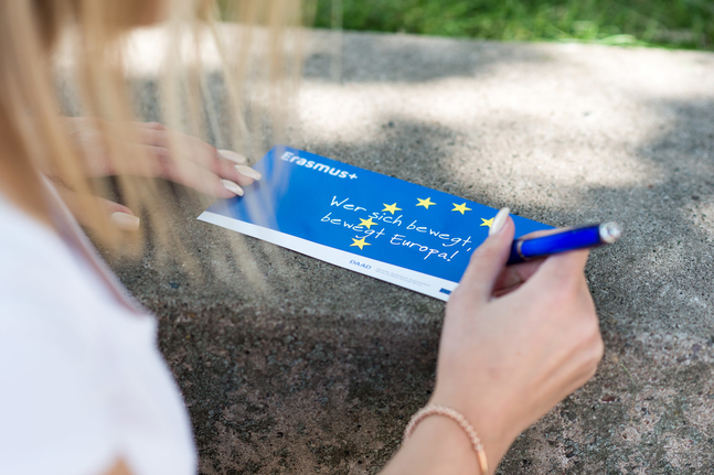 Rückenansicht einer Studentin mit Stift und Erasmus+ Karte