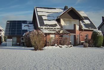 Ein Haus mit Photovoltaikmodulen auf dem Dach, die teilweise mit Schnee verdeckt werden
