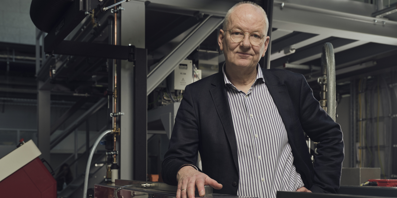 Porträtfoto von Prof. Dr. Christoph Jaroschek Im Hintergrund befindet sich eine Maschine für die Verarbeitung von Kunststoffgranulat