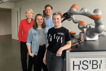Vier Personen stehen neben einem Roboterarm