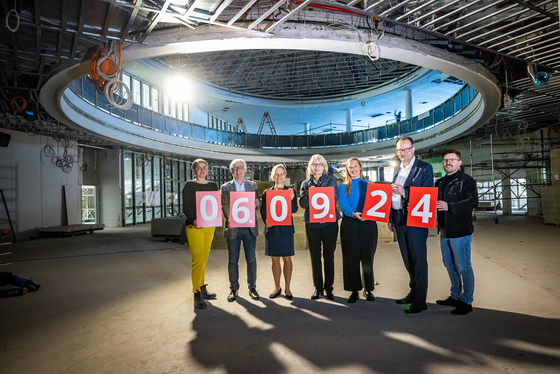 Acht Personen stehen in der Baustelle der zukünftigen Wissenswerkstadt. Sie halten Schilder mit Ziffern hoch, die das Datum 06.09.24 ergeben.