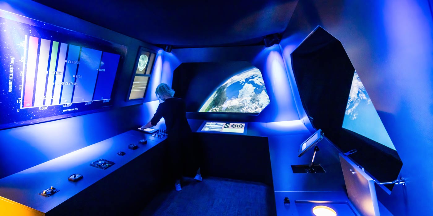 Ein Cockpit in blauem Licht. Durch die Scheiben ist der Weltraum und der Planet Erde zu sehen