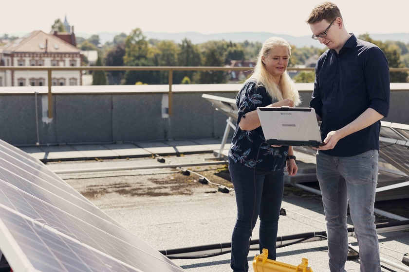 Prof. Dr. Grit Behrens und Felix Meyer stehen an der Photovoltaikanlage auf einem Dach