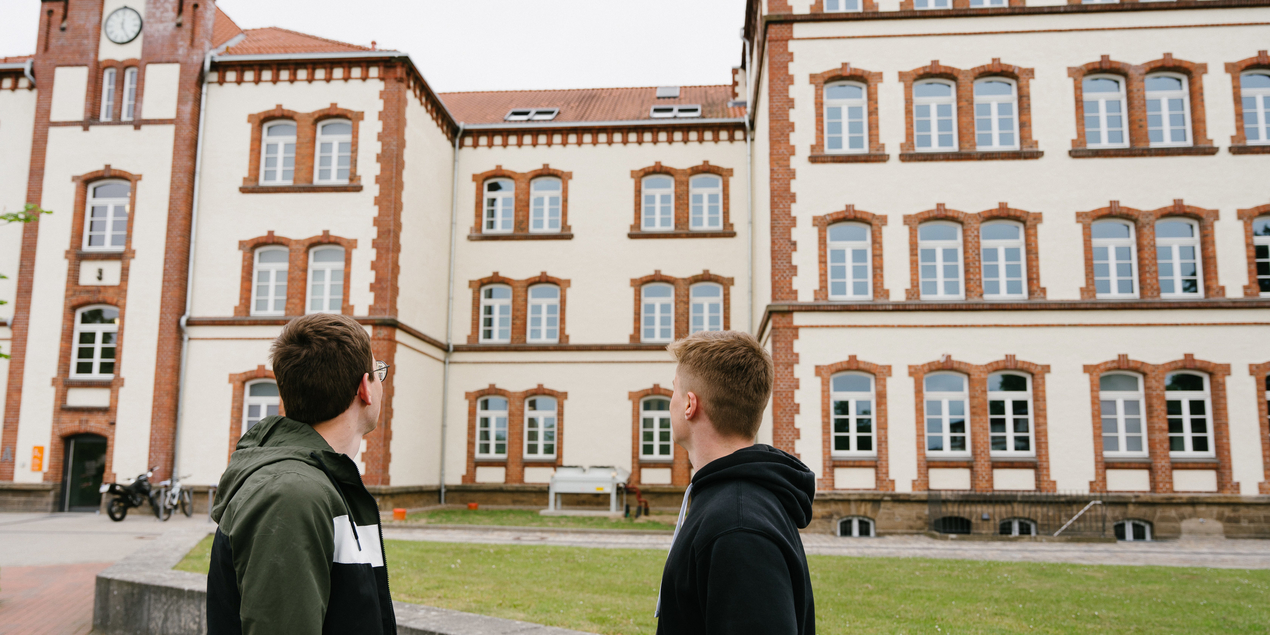 Zwei Studenten stehen auf dem Campus Minden und blicken zum Hauptgebäude.