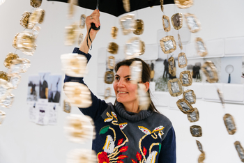 Eine Frau zeigt ein Kunstwerk Es ist ein Regenschirm an dem goldene Plättchen befestigt sind