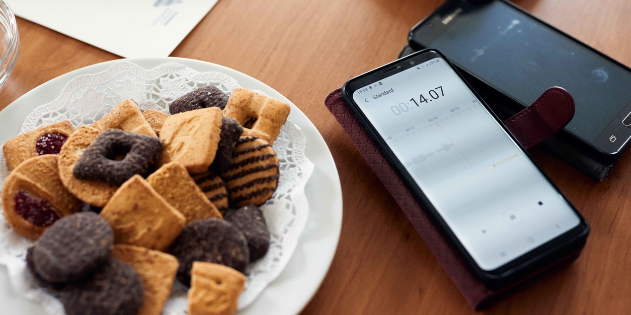 Auf einem Tisch steht ein Teller mit Plätzchen, daneben liegt ein Handy, auf dem gerade eine Audio-Datei aufgezeichnet wird.