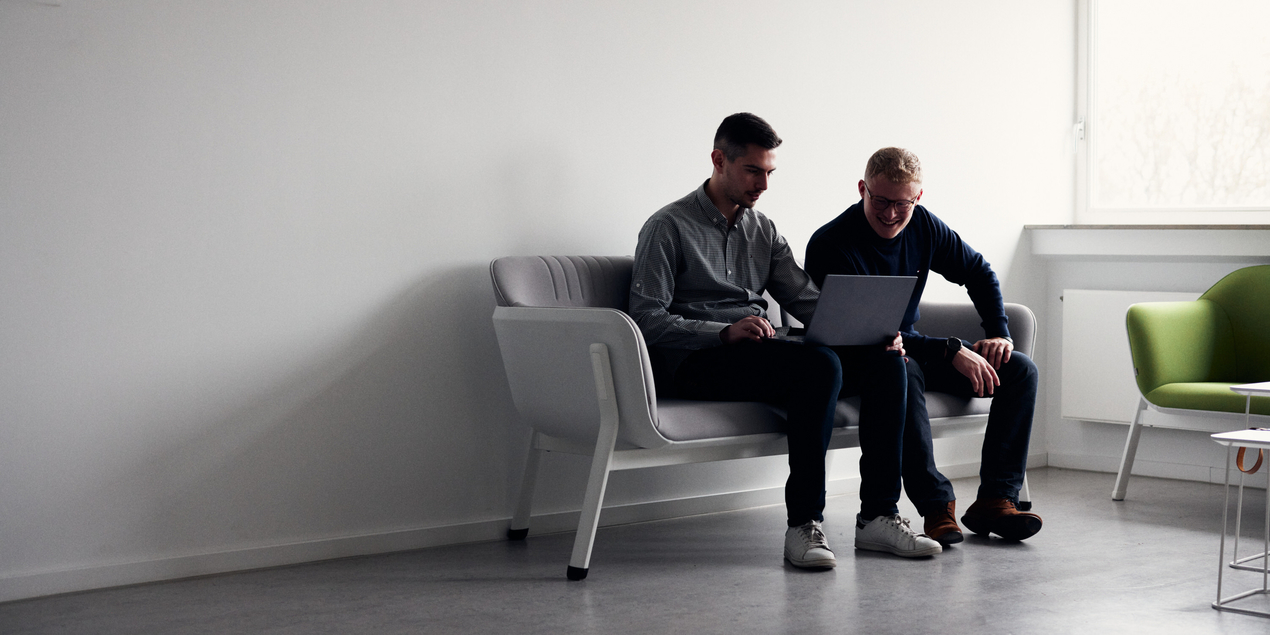 Tobias Patzer und Maik Abrams sitzen mit einen Laptop auf einer modernen Couch