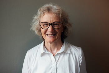 Porträtbild von Professorin Annette Nauerth von der HSBI die das Projekt Virdipa geleitet hat Die ältere Frau steht in einem weißen Hemd vor einem dunkelgrauen Hintergrund und lächelt direkt in die Kamera Sie trägt eine Brille mit schwarzem Gestell.