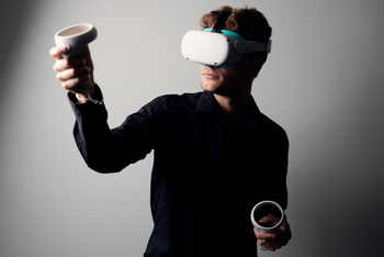 Ein Mitarbeiter des Virdipa Projekts erprobt mit einer aufgezogenen VR Brille die im Projekt entwickelten Übungsszenarien In seinen Händen hält er die Controller mit denen man sich innerhalb der virtuellen Welt bewegt