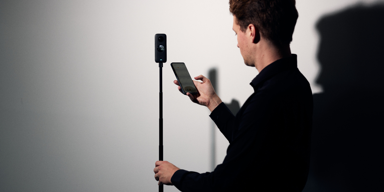 Ein Mitarbeiter des virdipa Projekts bedient mit einem Handy in seiner rechten Hand eine vor ihm auf einem Stativ stehende 360 grad Kamera